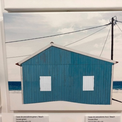 Pintura de casa de praia azul com janelas brancas, mar e céu ao fundo, pendurada na parede