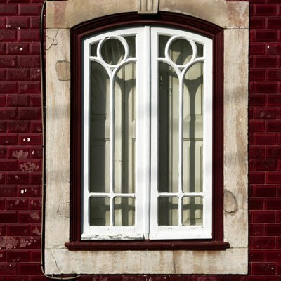 Janela branca de madeira com moldura de pedra numa parede com azulejos vermelhos