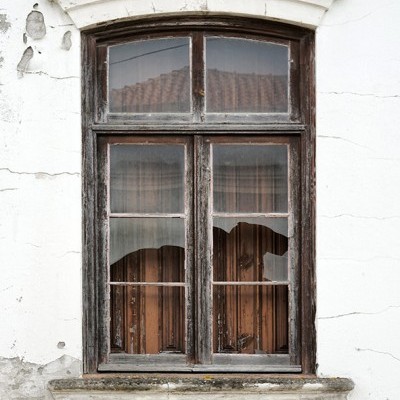 Janela antiga de madeira com vidro partido e parede branca rachada