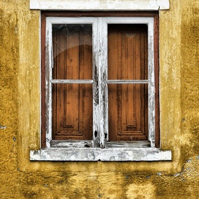 Janela de madeira branca desgastada com painéis castanhos em parede amarela texturada