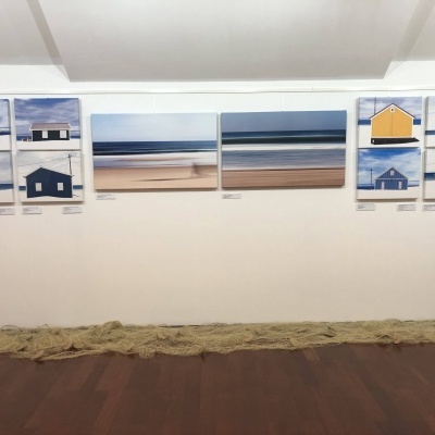 Fotografias de casas coloridas e paisagens marítimas expostas numa parede branca