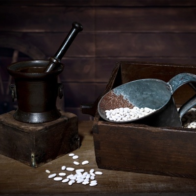 Almofariz, caixa de madeira e concha metálica com feijões brancos sobre mesa de madeira