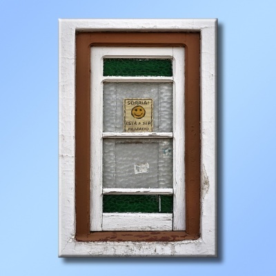 Janela de madeira branca e castanha com vidro fosco e verde e autocolante amarelo a dizer 