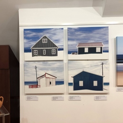 Quadros de casas junto ao mar em exposição artística com vasos de cerâmica ao lado
