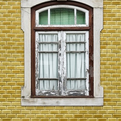 Janela de madeira lascada em parede de azulejos amarelos