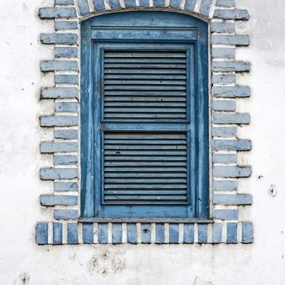 Janela de madeira azul com moldura de tijolos azuis e brancos numa parede branca