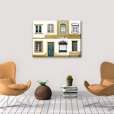 Sala com duas cadeiras castanhas, mesa de livros com vaso, puff castanho e quadro de janelas e portas na parede