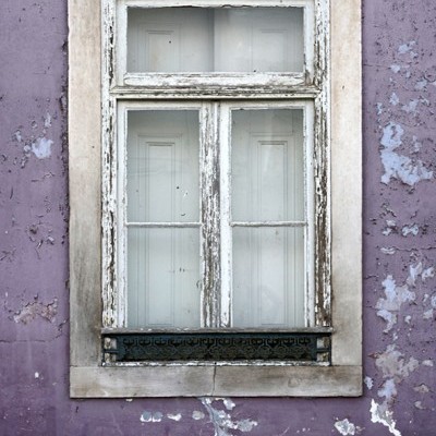 Janela velha com moldura de madeira branca numa parede roxa descascada