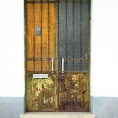 Porta dupla antiga com moldura branca, painéis de metal enferrujados e madeira amarelada