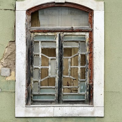 Janela velha de madeira com vidros partidos numa parede verde desgastada