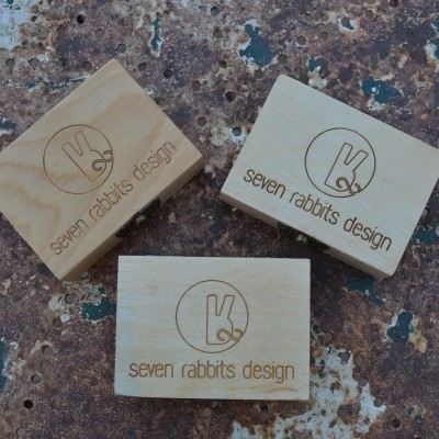 Três blocos de madeira com logo 'seven rabbits design' sobre superfície rugosa