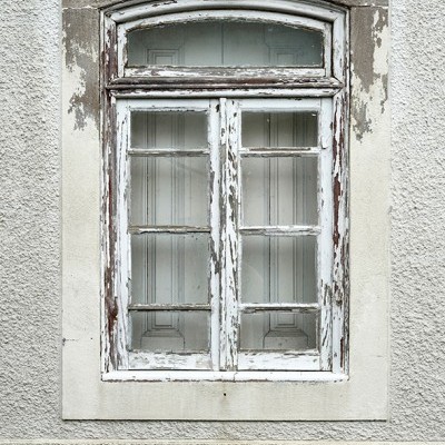 Janela de madeira branca antiga com pintura descascada numa parede cinza texturizada