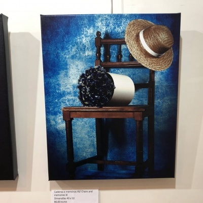 Cadeira de madeira escura com chapéu de palha e vaso preto sobre um fundo azul