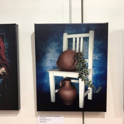 Quadro com cadeira branca, almofada castanha, planta e vaso castanho sobre fundo azul.