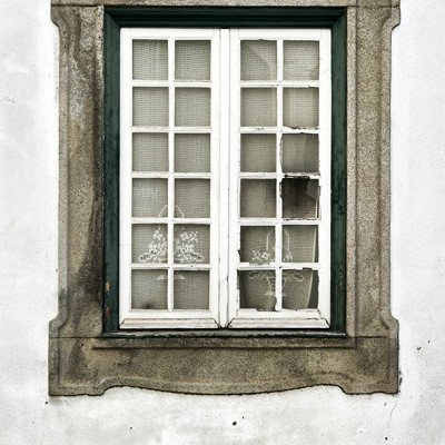 Janela antiga de madeira branca com vidros partidos e moldura de pedra cinzenta