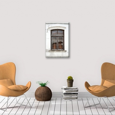 Dois cadeirões castanho claro com estruturas brancas, um cesto de vime, pilhas de livros com plantas, parede branca e janela decorativa.