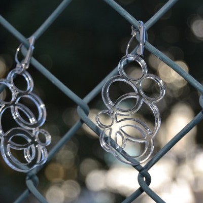 Dois pares de brincos prateados com anéis entrelaçados pendurados numa vedação metálica