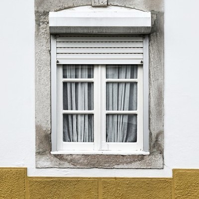 Janela branca com cortinas cinza em parede branca com base amarela