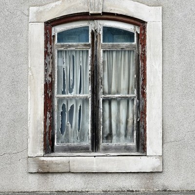 Janela antiga de madeira com cortinas brancas em parede cinzenta