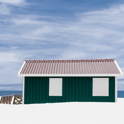 Casa pequena verde em madeira na praia com janelas cobertas e telhado vermelho