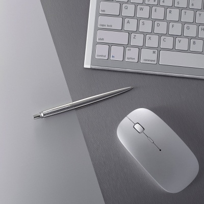 Teclado branco, rato branco e caneta metálica prateada sobre mesa cinzenta