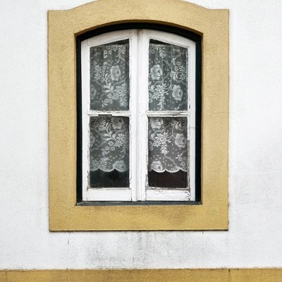 Janela branca com cortinas de renda e moldura amarela no muro
