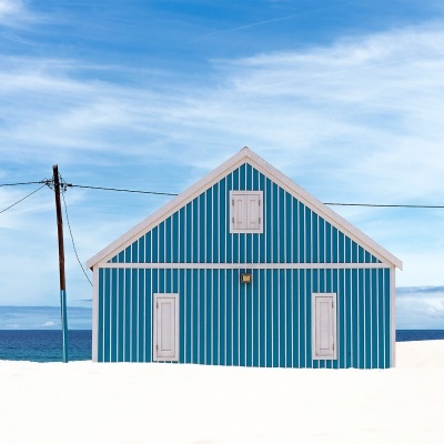Casa de praia azul e branca com riscas verticais na areia junto ao mar