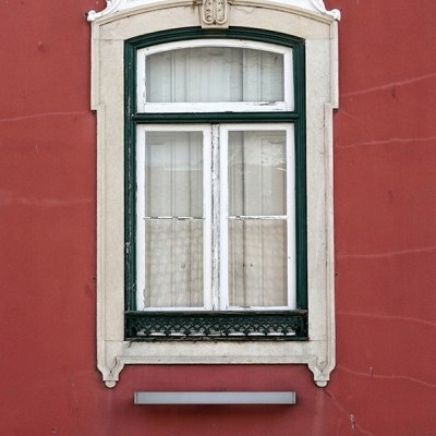 Janela verde com moldura branca e ornamento decorativo numa parede terracota