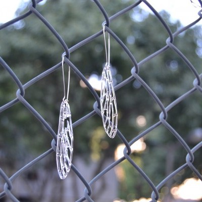 Brincos prateados de design em malha pendurados numa vedação metálica