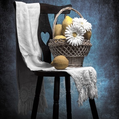 Cesto com peras e flores sobre cadeira de madeira preta com tecido branco