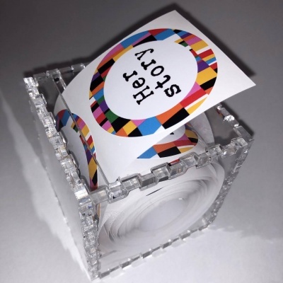 Suporte acrílico transparente em forma de cubo com cartão branco colorido com texto Her Story