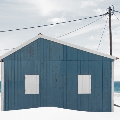 Casa de praia azul com janelas brancas em praia com areia branca e mar ao fundo