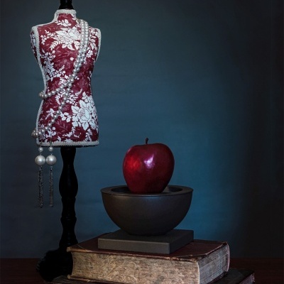 Maniquim decorativo com colar de pérolas, maçã vermelha em recipiente negro e livros antigos