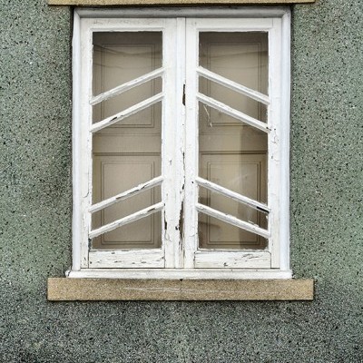 Janela dupla branca de madeira com barras horizontais em parede verde texturada