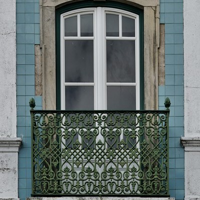 Janela branca dupla com varanda de ferro verde em fachada de azulejos azuis.