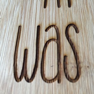 Gravação a laser da palavra 'was' numa superfície de madeira clara