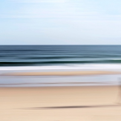 Praia com areia, mar e céu, com figura humana desfocada