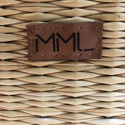 Etiqueta de couro castanho com texto 'MML_' numa cesta de verga bege claro