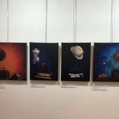 Quadros artísticos com gramofone, manequim, chapéu de palha e livros em parede branca