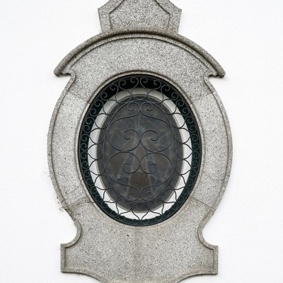 Janela oval com moldura de pedra cinzenta e grade metálica preta