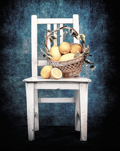 Cadeira branca rústica com cesta de limões e folhas secas