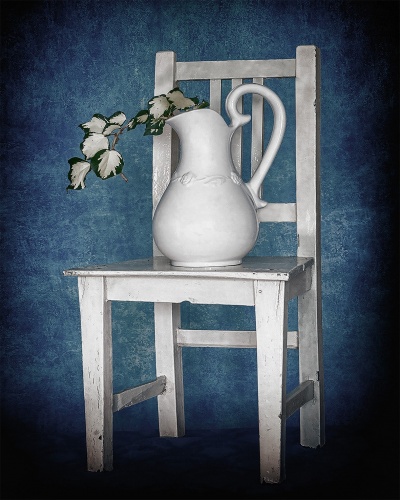 Cadeira branca de madeira com jarro branco contendo ramo com folhas