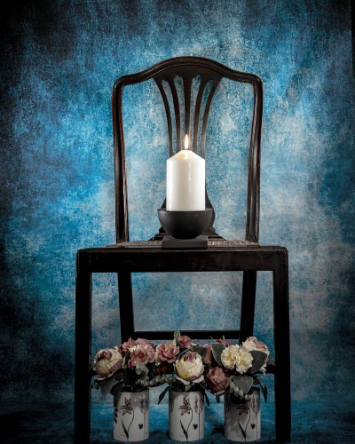 Cadeira de madeira escura com vela acesa e vasos de flores