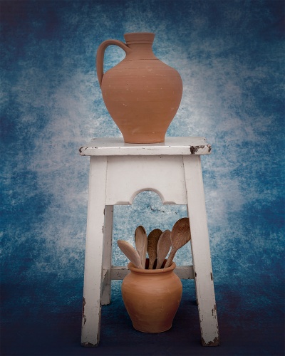 Dois jarros de barro castanho com colheres de madeira em banco branco com fundo azul.