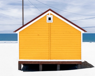 Casa pequena de praia amarela sobre pilares na areia com mar ao fundo
