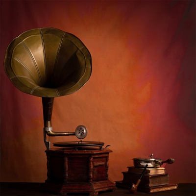 Gramofone vintage de latão e madeira com moedor manual de café e livros num fundo alaranjado.