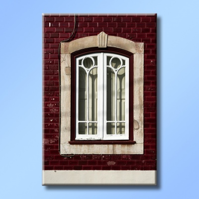 Janela com moldura de pedra e caixilhos brancos numa parede de tijolos vermelhos