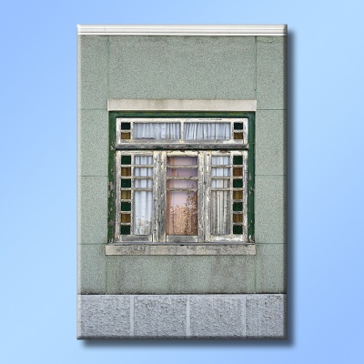 Janela de madeira verde gasta com vidro decorativo e cortinas brancas numa parede de pedra verde e cinzenta