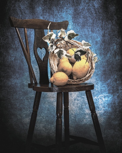 Cadeira de madeira com cesta de verga contendo frutos amarelos e folhas artificiais