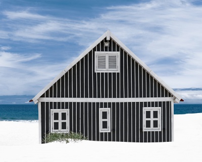 Casa de praia preta com riscas brancas na praia com mar e céu azul